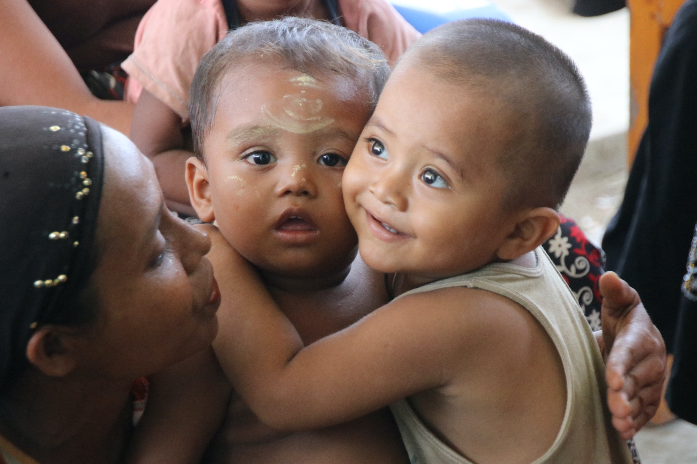 A toddler hugging another toddler and a Rohingya Muslim who is some sort of mother or some guardian is looking with a smile.